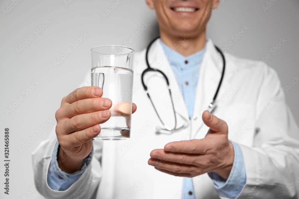 Nutritionist holding glass of pure water on light grey background, focus on hand Nutritionist holding glass of pure water on light grey background, focus on hand