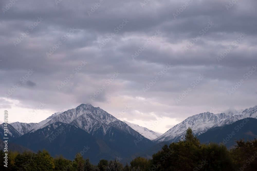 Mountains cowered with snow and cloudy sky background. Bad weather concept.