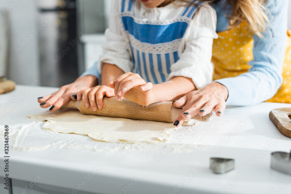 cropped view of mother and daughter rolling dough on table