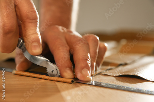 Man marking leather with roller in workshop, closeup