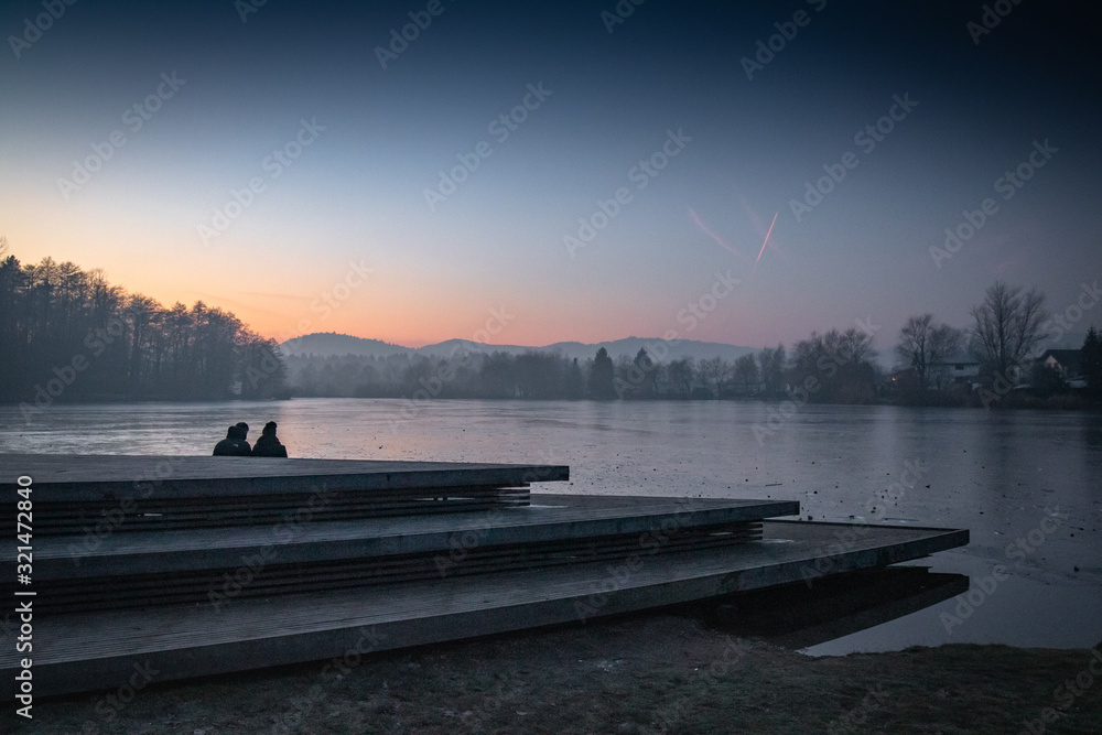 silhouette of couple people enjoying sunset view on freezing cold lake, slovenia