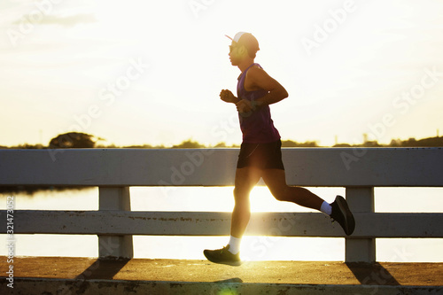 Attractive fit man running fast along bridge at sunset light