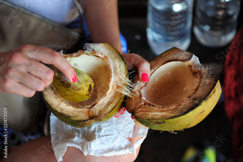 Eating a green coconut, indian traditional way without spoon or tools. Close-up of woman hands in process of scraping the coconut flesh from peel.