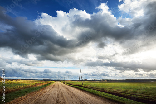 Storm clouds above the empty dirt road. Agricultural fields and forest in the background. Warm evening sunlight. Baltic sea, Garciems, Latvia photo