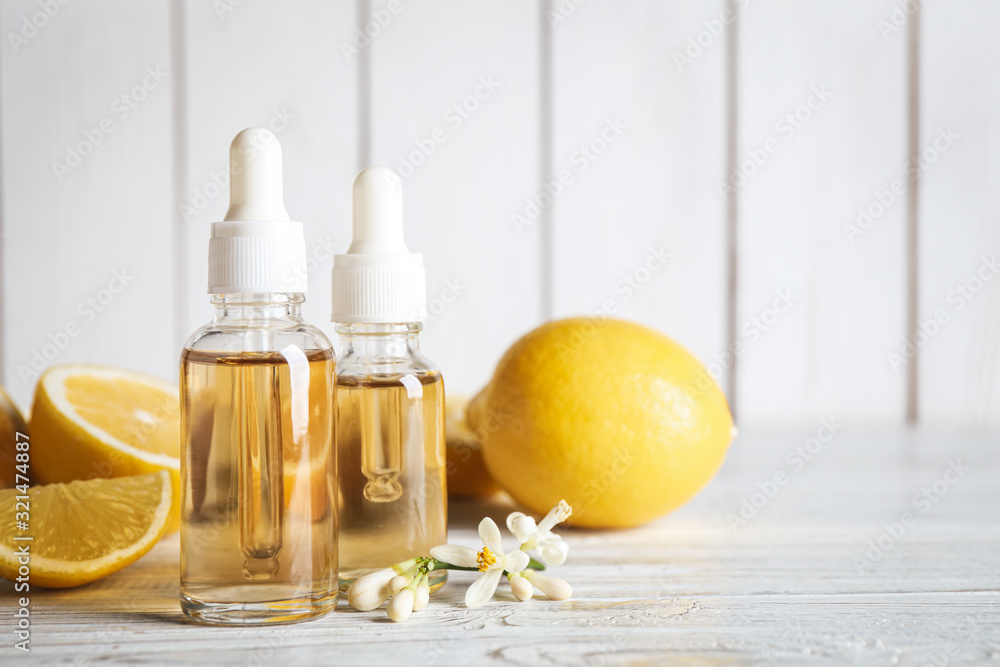 Bottles of citrus essential oil, flower and lemons on white wooden table. Space for text Bottles of citrus essential oil, flower and lemons on white wooden table. Space for text