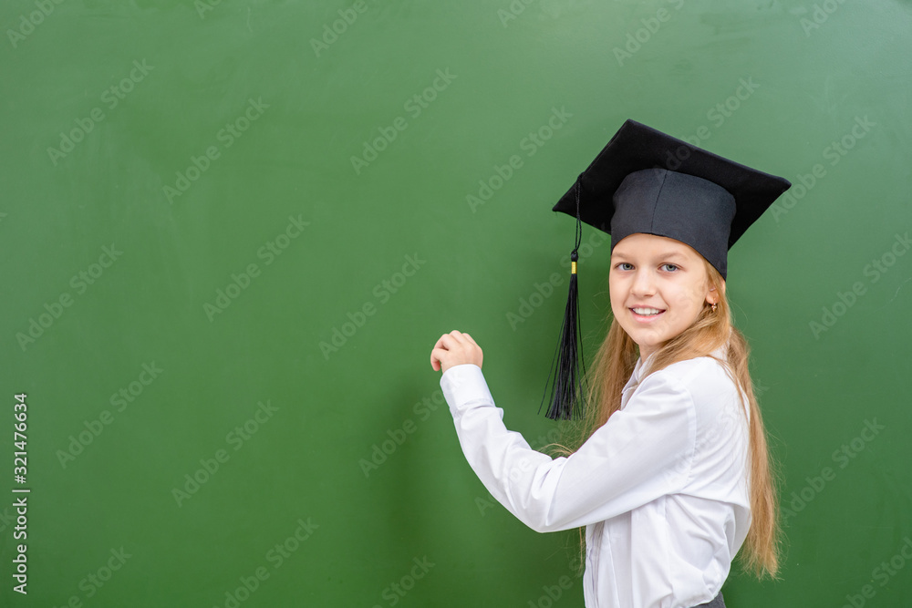 Young girl wearing a graduation cap writing on a chalkboard. Education and school concept Young girl wearing a graduation cap writing on a chalkboard. Education and school concept