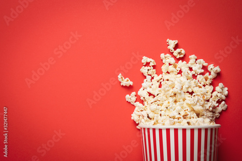 Overturned paper cup with delicious popcorn on red background, top view. Space for text