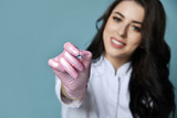 Portrait of smiling brunette woman doctor cosmetologist in pink medical gloves and uniform holding accessories