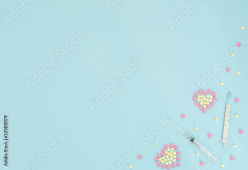Two hearts made of pink and yellow pills, thermometer, syringe on light blue background. Seasonal diseases. Medicine concept. Flat lay style with copy space, top view. © Rina Mskaya