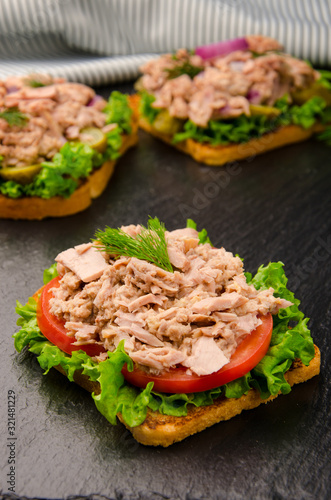 Tuna sandwiches with lettuce tomatoes pickles and onions on slate