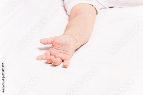 Clouse-up photo of little infant hand laying on the bed sheet