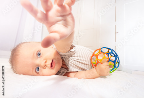Little infant baby stretch with hand to the camera laying on the side on the bed