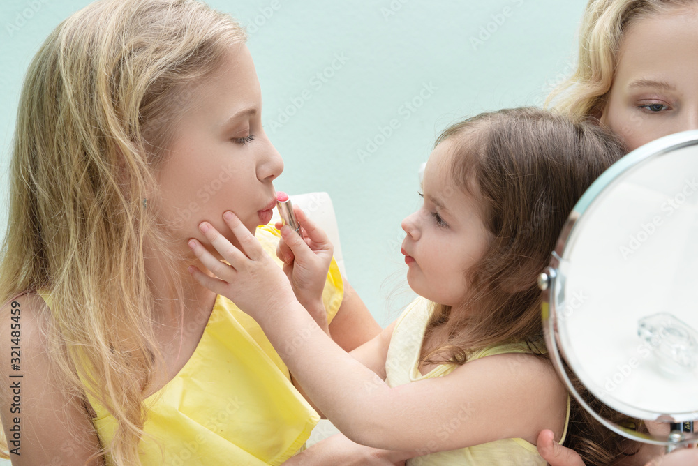 Young sisters sitting at a table makes herself a make-up Young sisters sitting at a table makes herself a make-up