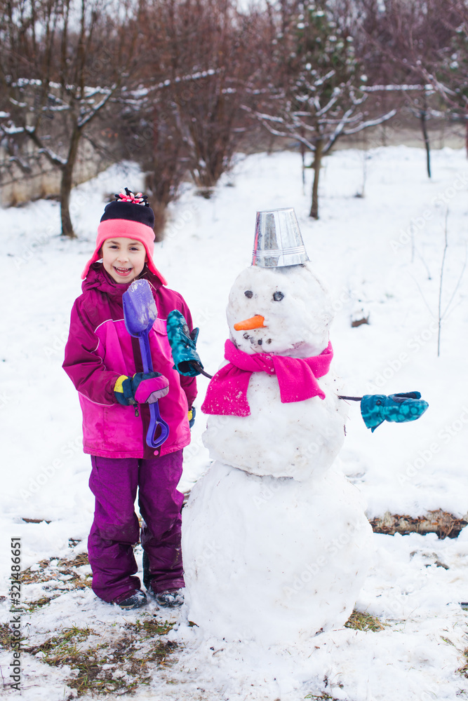 Pretty little girl in warm outwear maked snowman in cold frosty day Pretty little girl in warm outwear maked snowman in cold frosty day
