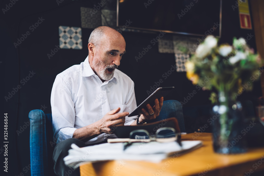 Shocked senior man looking at tablet screen with opened mouth Shocked senior man looking at tablet screen with opened mouth
