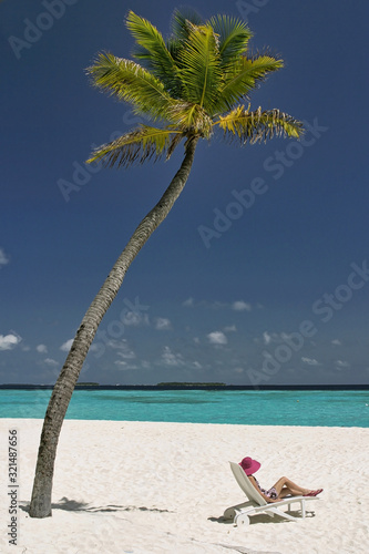 Relaxing under a Maldives palm tree on a white sand beach with perfect turquoise ocean background. Travel destination or relaxation concept.