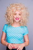 Beautiful retro-style blonde girl with voluminous curly hairstyle, in a blue polka-dot blouse on a gray background, smiles and looks at the camera