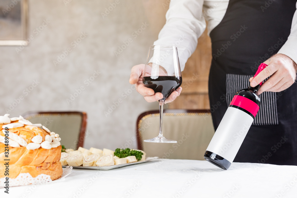 Fototapeta premium Man holding wine and decorated bread on table for celebration a saint in Orthodox faith. Serbian traditional and cultural heritage.