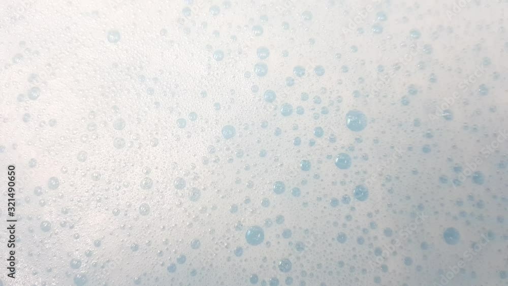 White foam with bubbles popping in blue water, closeup. White foam with bubbles popping in blue water, closeup.