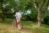 Shot of an  woman walking with a bicycle through a garden or through a forest.  She enjoys the beautiful environment.