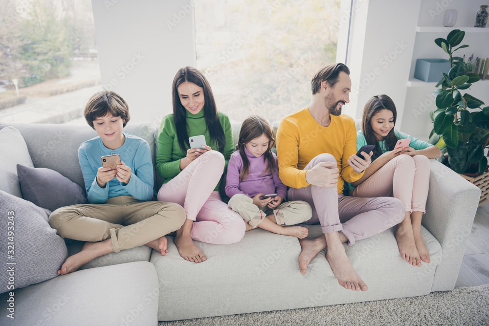 Portrait of nice attractive bare foot big full cheerful cheery family pre-teen kids spending free time sitting on sofa using 5g app internet online wi-fi connection at light white interior style house Portrait of nice attractive bare foot big full cheerful cheery family pre-teen kids spending free time sitting on sofa using 5g app internet online wi-fi connection at light white interior style house
