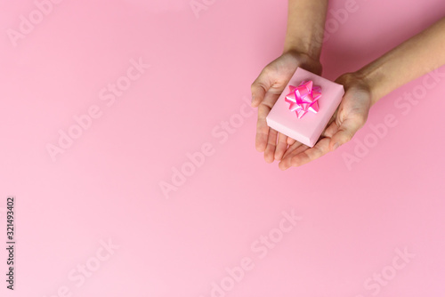 Hands with pink gift box with beautiful rose bow on pink background. St. Valentines day concept. Gift concept. Copy space for your text.