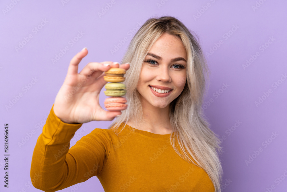 Teenager girl over isolated purple background holding colorful French macarons and with happy expression Teenager girl over isolated purple background holding colorful French macarons and with happy expression