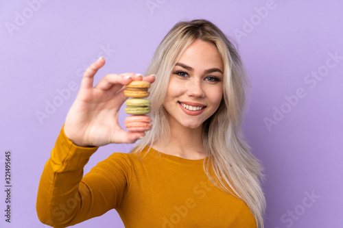 Teenager girl over isolated purple background holding colorful French macarons and with happy expression