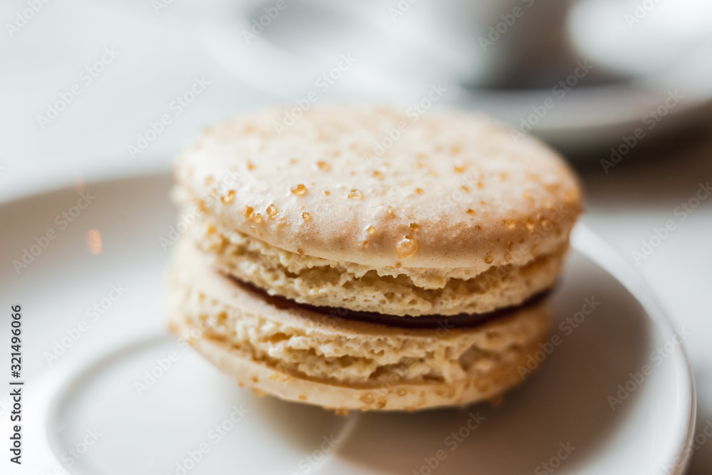 A close up photo of a macaron with salted caramel on a white saucer, a cup of coffee in the background A close up photo of a macaron with salted caramel on a white saucer, a cup of coffee in the background