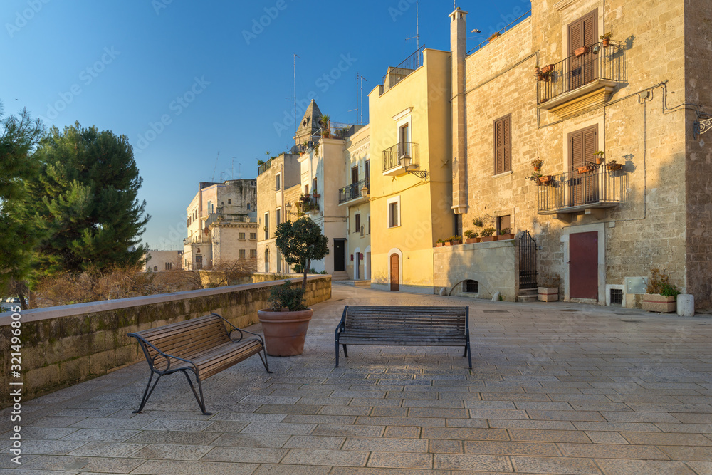 View of a beautiful alley with two benches in front of buildings illuminated by the rising sun near the sea in Bari, Italy