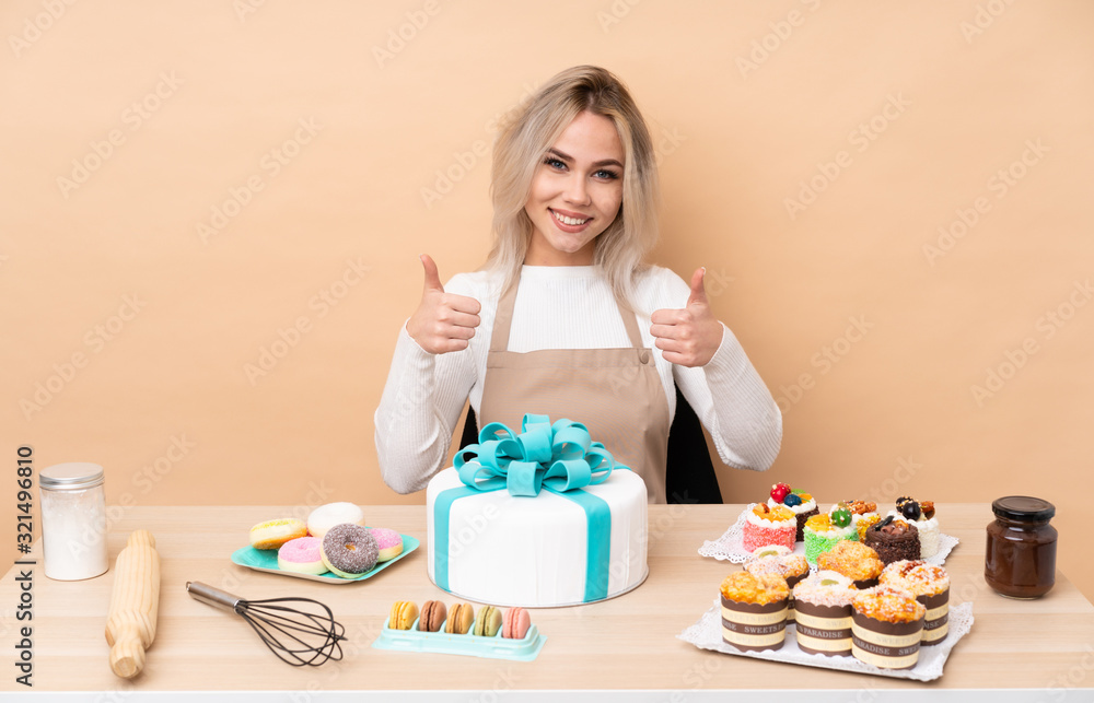 Teenager pastry chef with a big cake in a table giving a thumbs up gesture Teenager pastry chef with a big cake in a table giving a thumbs up gesture