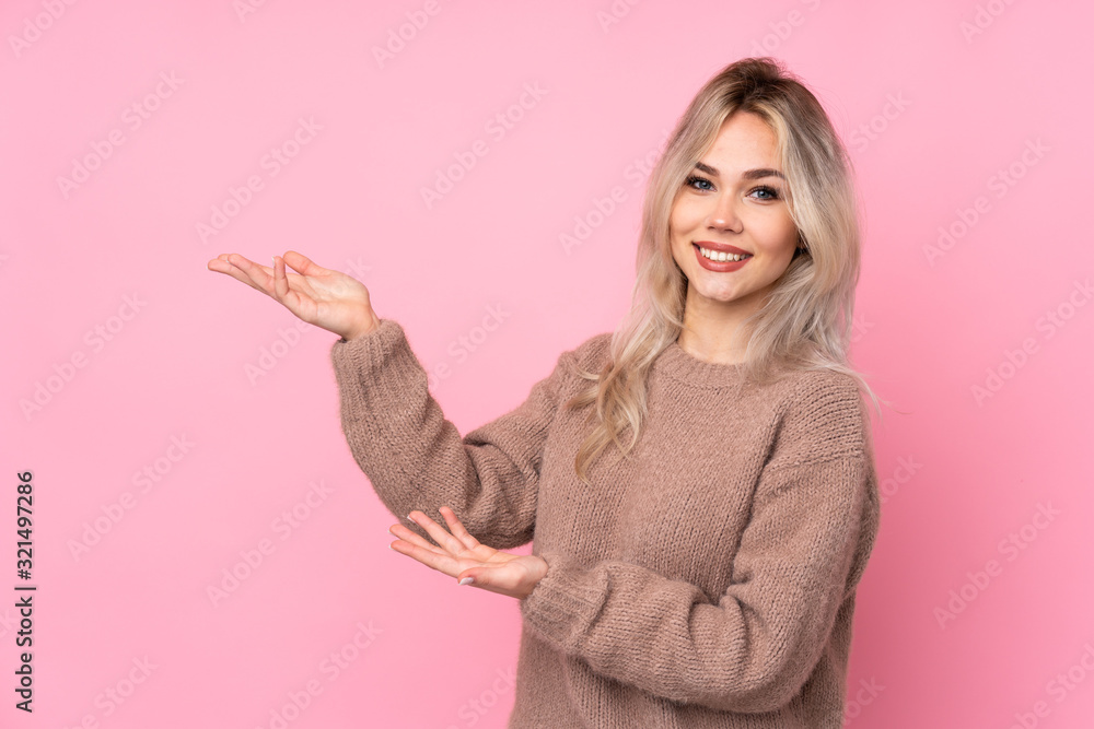 Teenager blonde girl wearing a sweater over isolated pink background extending hands to the side for inviting to come Teenager blonde girl wearing a sweater over isolated pink background extending hands to the side for inviting to come