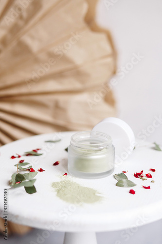 Powder cosmetic mask. Glass jar with matcha on a white background with dry petals.