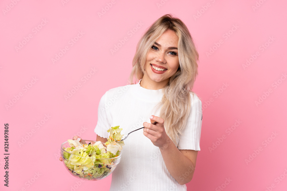 Teenager blonde girl holding a salad over isolated pink wall Teenager blonde girl holding a salad over isolated pink wall