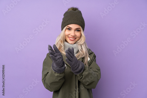 Teenager blonde girl with winter hat over isolated purple background applauding after presentation in a conference