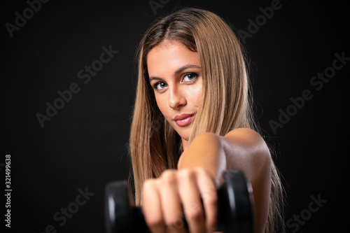 Young sport blonde woman making weightlifting over isolated black background