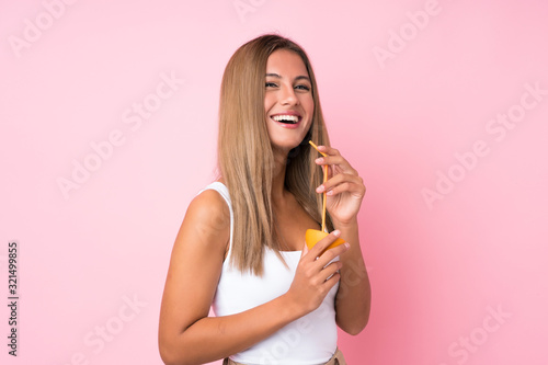 Young blonde woman over isolated background holding an orange