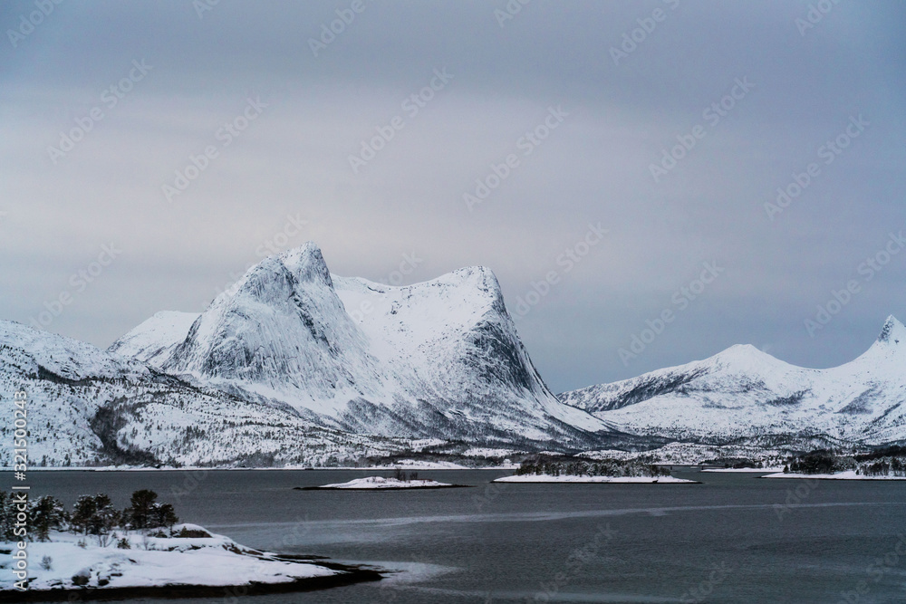 Spectacular winter landscape shoot in northern Norway. Mountains covered with snow near a fjord, overcast sky.