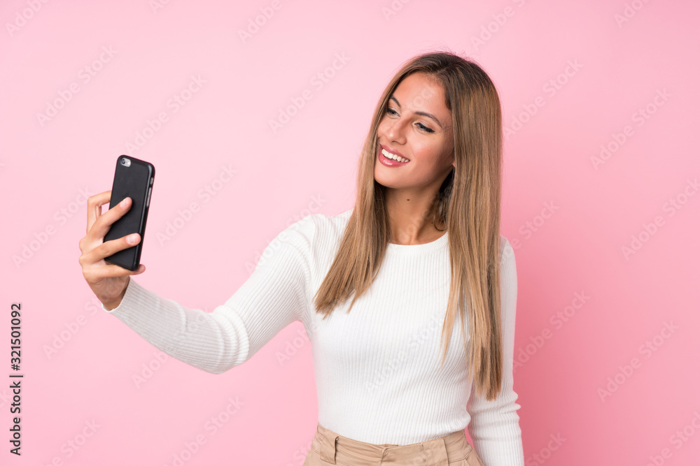 Fototapeta premium Young blonde woman over isolated pink background taking a selfie with the mobile