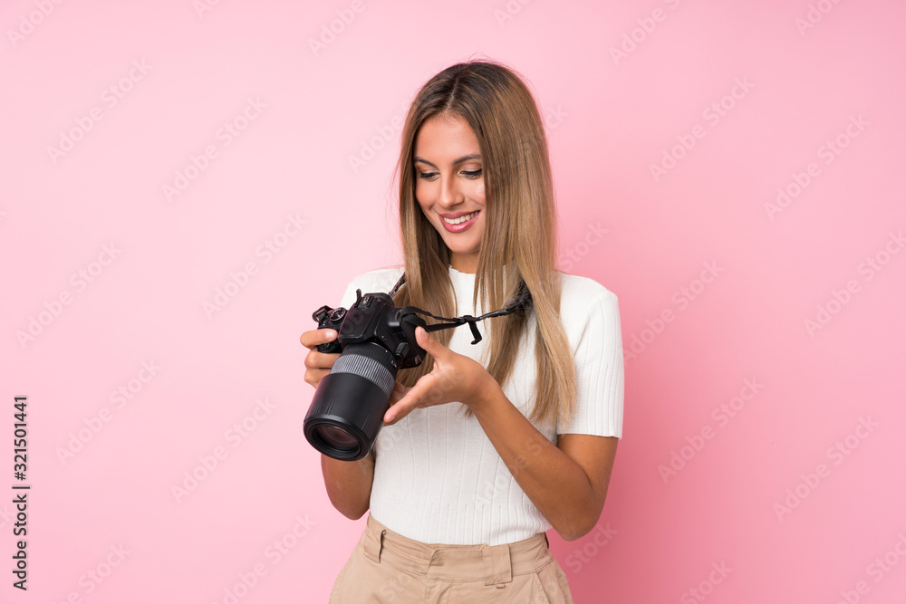 Young blonde woman over isolated pink background with a professional camera Young blonde woman over isolated pink background with a professional camera