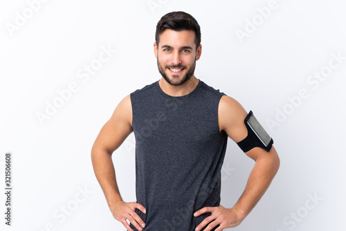 Young sport handsome man with beard over isolated white background posing with arms at hip and smiling