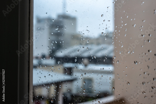 Window on a rainy day with small drops in it. Focus on the small drops with shallow depth of field and a visual of city buildings.