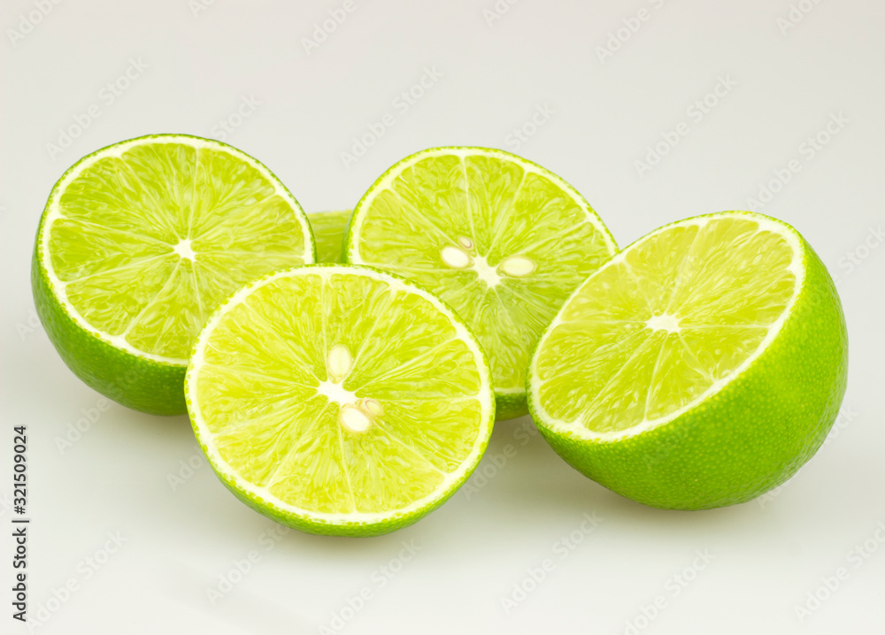 Lime is a natural green lime that is cut in half and thin, green leaves on a white background.