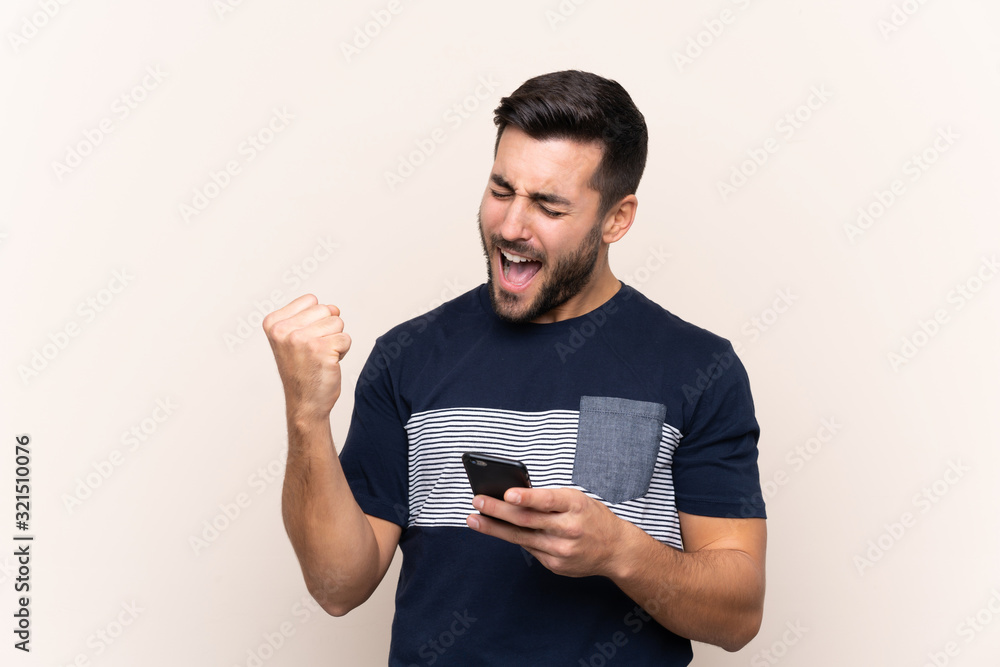 Young handsome man with beard over isolated background with phone in victory position Young handsome man with beard over isolated background with phone in victory position