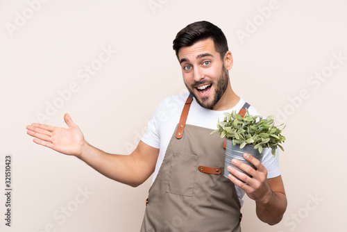 Gardener man holding a plant over isolated background extending hands to the side for inviting to come