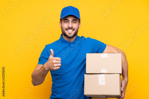 Delivery man over isolated yellow background with thumbs up because something good has happened photo