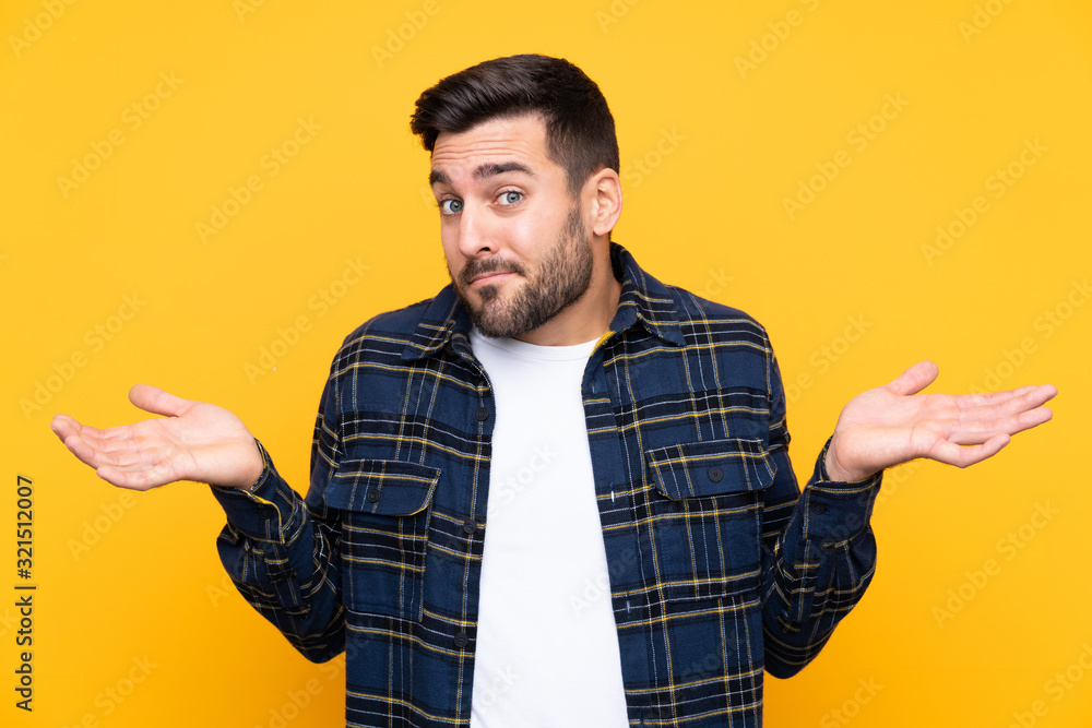 Young handsome man with beard over isolated yellow background having doubts while raising hands Young handsome man with beard over isolated yellow background having doubts while raising hands