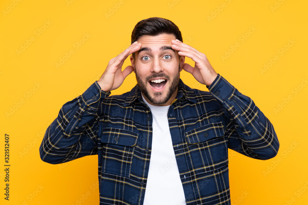 Young handsome man with beard over isolated yellow background with surprise expression Young handsome man with beard over isolated yellow background with surprise expression