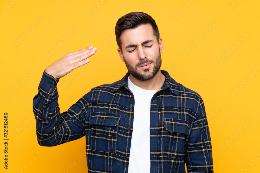 Young handsome man with beard over isolated yellow background with tired and sick expression Young handsome man with beard over isolated yellow background with tired and sick expression