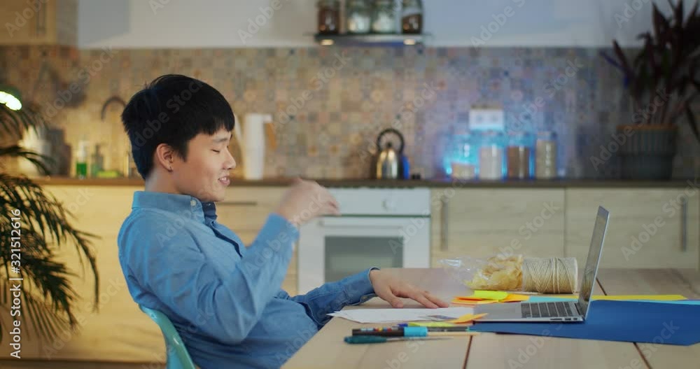 Handsome Asian guy sitting behind table using laptop successful happy moment indoors, young millennial creative man dressed in blue shirt working online in network at cozy kitchen leaning back on Handsome Asian guy sitting behind table using laptop successful happy moment indoors, young millennial creative man dressed in blue shirt working online in network at cozy kitchen leaning back on
